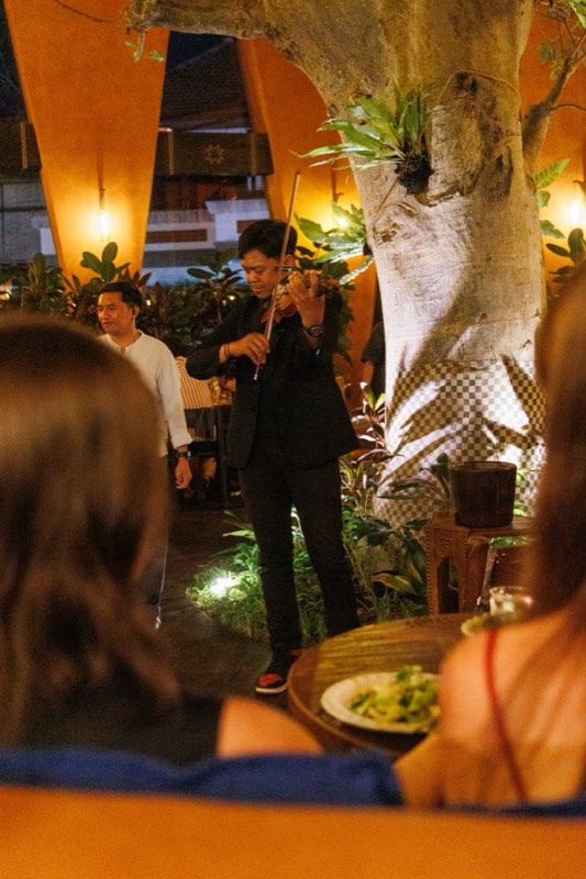 A violinist playing between tables beside the baobab during Thursday violin night